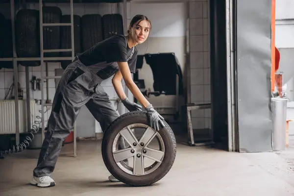 stock image Smiling Charming Woman Car mechanic holding tire at repair garage. Replacement of winter and summer tires