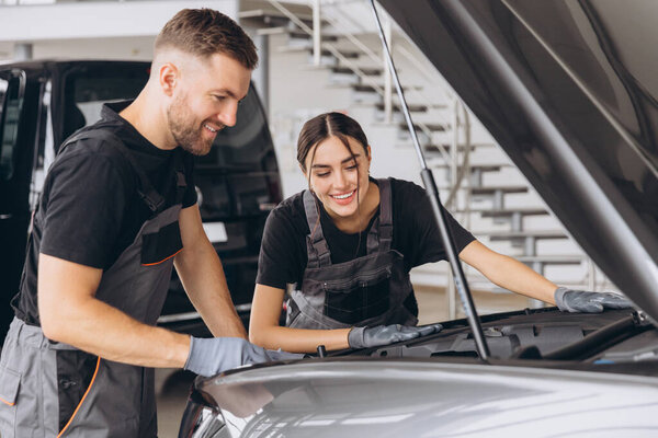 Пытаюсь идентифицировать источник проблемы. Два механика мужчина и женщина работают вместе на открытом капоте над машиной в автомастерской.