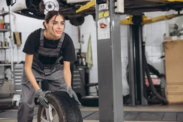 stock image Smiling Charming Woman Car mechanic holding tire at repair garage. Replacement of winter and summer tires