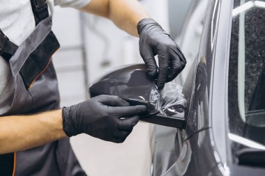 Eldivenli bir teknisyen arabanın yan aynasına koruyucu film uyguluyor, bir oto atölyesinde hassasiyet ve bakım gösteriyor..