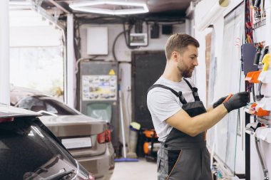 Tamirci, garaj atölyesinin duvarındaki aletleri düzenleyen eldivenler giyiyor. Profesyonel bir otomotiv tamir ayarında verimliliğe odaklanmış.