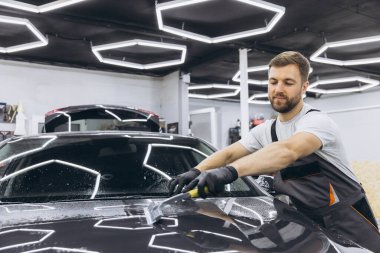 Adam araba kaputunu yıkıyor ve cam kaplama parlatma işlemini hazırlıyor. Erkek işçi garaja koruma filmi yerleştiriyor. Araç Ayrıntıları.