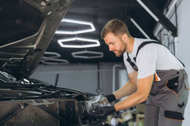 Modern bir otomotiv tamirhanesinde bir arabanın farını tamir etmeye çalışan yetenekli bir tamirci. Tulum ve eldivenler konusunda uzman..