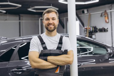 Kendine güvenen bir tamirci modern bir garajda profesyonellik ve uzmanlık göstererek gururla duruyor. Görüntü, iyi donanımlı ve verimli bir çalışma alanının atmosferini yansıtıyor..