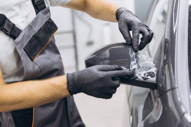 Eldivenli bir teknisyen arabanın yan aynasına koruyucu film uyguluyor, bir oto atölyesinde hassasiyet ve bakım gösteriyor..