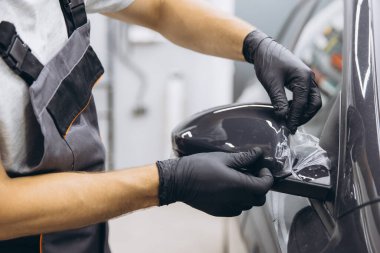 Eldivenli bir teknisyen arabanın yan aynasına koruyucu film uyguluyor, bir oto atölyesinde hassasiyet ve bakım gösteriyor..