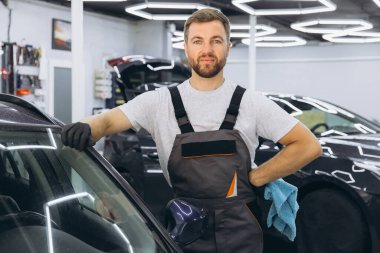Araba temizliği, yıkama ve temizlik konsepti. Siyah lastik eldivenli, genç, sakallı, profesyonel araba yıkayıcı. Mikrofiber tutuyor ve lüks araba siliyormuş..