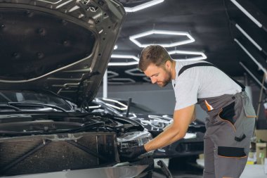 Modern bir otomotiv tamirhanesinde bir arabanın farını tamir etmeye çalışan yetenekli bir tamirci. Tulum ve eldivenler konusunda uzman..