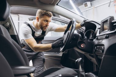 Bir tamirci dükkanında çalışıyor ve bir araba servisinin direksiyonunu kontrol ediyor..