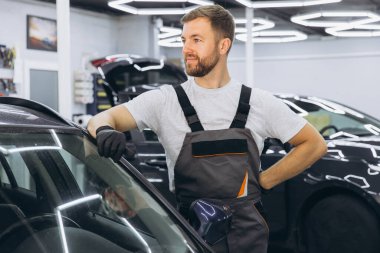 Modern bir garajda, tulumlu, gülümseyen bir araba tamircisi. Araçlar ve tamirat konusunda profesyonel uzmanlık. Otomotiv endüstrisi işçisi. Cihazları ve ekipmanları var..