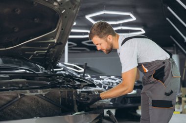 Modern bir otomotiv tamirhanesinde bir arabanın farını tamir etmeye çalışan yetenekli bir tamirci. Tulum ve eldivenler konusunda uzman..