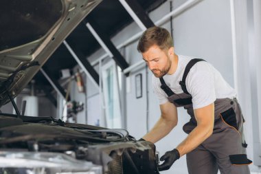 Modern bir otomotiv tamirhanesinde bir arabanın farını tamir etmeye çalışan yetenekli bir tamirci. Tulum ve eldivenler konusunda uzman..