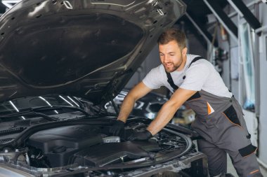 Tulum giyen mutlu oto tamircisi iyi aydınlatılmış bir garajda araba motorunda çalışıyor. Sahne, araç bakımında uzmanlık ve adanmışlığı yakalıyor.