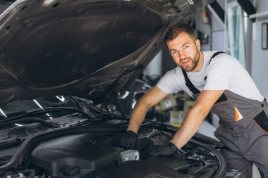 Tulum giyen mutlu oto tamircisi iyi aydınlatılmış bir garajda araba motorunda çalışıyor. Sahne, araç bakımında uzmanlık ve adanmışlığı yakalıyor.