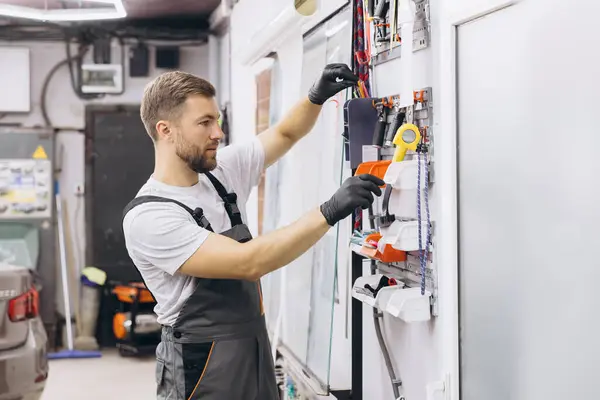 stock image Mechanic wearing gloves organizing tools on a wall rack in a garage workshop. Focused on efficiency in a professional automotive repair setting.