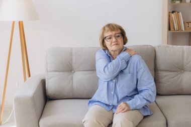 Koltuğunda oturan yaşlı kadın omuz ağrısı çekiyor. Yaşlı kadın korkunç bir ağrıya katlanıyor. Omzundan yaralanan yaşlı kadın, sağlık sorunu kavramı.