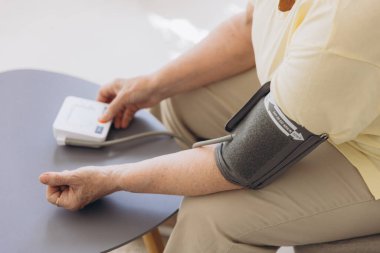 Yüksek tansiyonu olan son sınıf öğrencisi bir kadın evinde tansiyonunu ölçüyor. Üzgün yaşlı kadın kan basıncını tonometreyle ölçüyor.. 