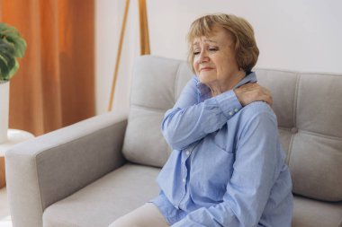 Koltuğunda oturan yaşlı kadın omuz ağrısı çekiyor. Yaşlı kadın korkunç bir ağrıya katlanıyor. Omzundan yaralanan yaşlı kadın, sağlık sorunu kavramı.