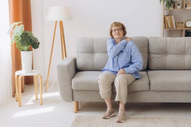 Koltuğunda oturan yaşlı kadın omuz ağrısı çekiyor. Yaşlı kadın korkunç bir ağrıya katlanıyor. Omzundan yaralanan yaşlı kadın, sağlık sorunu kavramı.