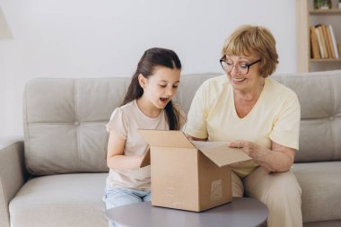 Karton kutuyu açan mutlu büyükanne ve torun kızı evdeki kanepede oturuyor. Şok olmuş aile tüketicileri iyi paketleri açıyor ve büyük alışverişin içine bakıyor..