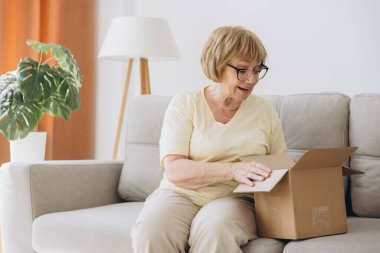 Kanepenin üstünde oturan mutlu yaşlı kadın paket paketi, internet siparişi, tıbbi malzeme, hap, vitamin, ilaç, uyuşturucu aldı..