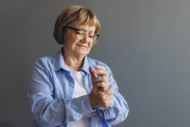 Elderly woman suffering from pain in hand, close up on gray background clipart