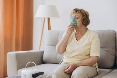 Hasta yaşlı kadın viral enfeksiyon ya da grip, nefes darlığı, astım. Yaşlı bir kadın solunum cihazını kullanıyor, nebulizatör de kendini tedavi etmek için evde tek başına oturuyor.