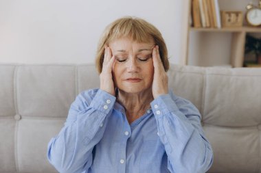 Evdeki kanepede oturan yaşlı bir kadının portresi. Baş ağrısı, ağrı ve kendini kötü hissetme ifadesi.