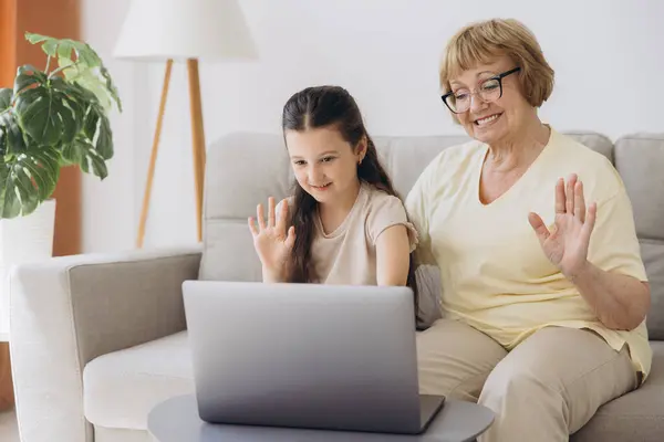 stock image Granddaughter with grandmother waving hand during video call. Old woman sitting with her little granddaughter making a video call.