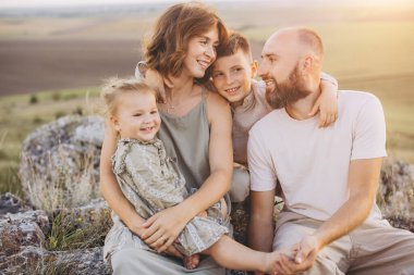Doğada dört kişilik gülümseyen aile gün batımında güzel bir kırsal alanda aileleri ve çocukları kucaklıyor..