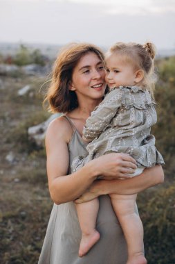 Şefkatli bir anne, genç kızını sakin bir açık hava ortamında kucaklar. Güzel bir altın saat boyunca sevgi ve mutluluk taşır..