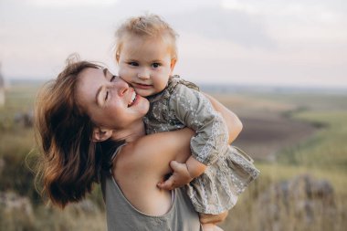 Neşeli bir anne, genç kızını dışarıda kucaklıyor. Huzurlu bir kırsal alanda mutluluk ve aile sevgisini yakalıyor..
