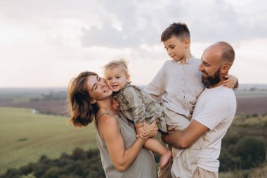 Dört kişilik neşeli bir aile, ebeveynleri ve iki çocuğu olan, doğal manzaralı bir ortamda birlikte mutlu bir an geçiriyorlar..