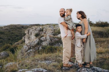 İki çocuklu neşeli bir aile uçurumun kenarında, doğanın ve açık havanın tadını çıkarıyor, mutluluk ve sevgi saçıyor..