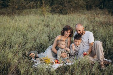 Dört kişilik neşeli bir aile yemyeşil bir çayırda piknik yapıyor. Güneşli bir günde birlikte güzel vakit geçiriyorlar..