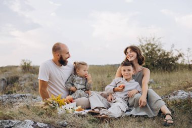 Manzaralı bir alanda piknik yaparken gülümseyen dört kişilik bir aile. Ebeveynler ve çocuklar birlikte kaliteli zaman geçirmeyi severler, neşeli ve kaygısız anları yakalarlar..