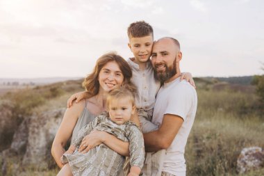 Dört kişilik neşeli bir aile, gün batımında manzaralı bir yerde, doğada sıcaklığı ve birlikteliği yakalıyorlar..
