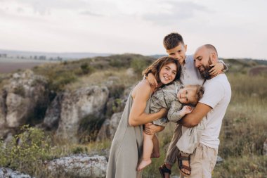 Gülümseyen dört kişilik aile, güzel bir açık hava ortamında birbirlerini kucaklıyor, bir yaz günü boyunca mutluluk ve beraberlik anları yakalıyorlar..