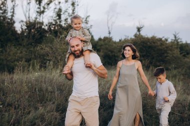 Doğada gezen mutlu bir aile, ebeveynler ve iki küçük çocukla birlikte açık havada kaynaşma deneyimi yaşıyorlar. Manzaranın ortasındaki sevgi, birliktelik ve neşeyi vurgular.