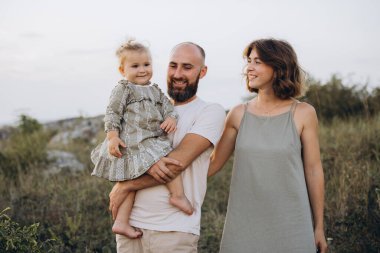 Neşeli bir aile dışarıda iyi vakit geçiriyor. Gülümseyen bebeğini kucağında taşıyan bir baba, yanında annesi olan, resmedilmeye değer doğal bir manzara..