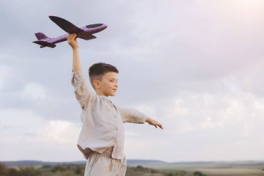 Dışarıda oyun oynamaktan hoşlanan küçük bir çocuk, uçağını engin bulutlu bir gökyüzüne doğru tutuyor, macera ve çocukluk hayalinin ruhunu somutlaştırıyor..