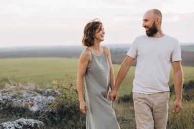 Gülümseyen bir çift sakin kırsalda yürürken el ele tutuşuyor. Neşeli ve rahat görünüyorlar, bu güzel manzaranın ortasında birbirlerinin arkadaşlığından keyif alıyorlar..