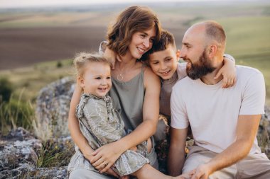 Dört kişilik neşeli bir aile kırsal alanda sıcak bir anı paylaşıyor. Ebeveynler ve çocuklar, beraberlik ve mutluluğu vurgulayarak huzurlu ve huzurlu doğanın tadını çıkarıyorlar..