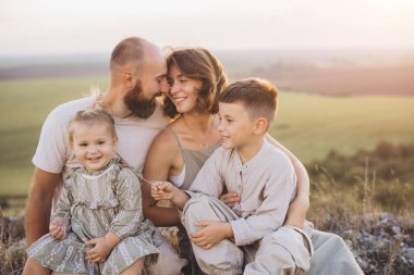 Neşeli aile, doğa ve güneş ışığıyla çevrili harika açık havada birlikte vakit geçiriyorlar. Mutluluk ve beraberlik sergiliyorlar..