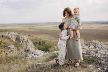 Anne, oğlu ve kızıyla birlikte kırsal manzaranın tadını çıkarıyor, neşe ve bağlantı anlarını paylaşıyor..