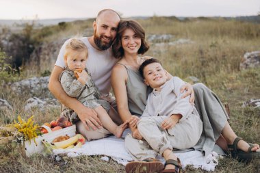 Dört kişilik mutlu bir aile piknik battaniyesinde birlikte oturur. Etrafı doğa ile çevrilidir. Dışarıda huzurlu bir günün tadını çıkarırlar..