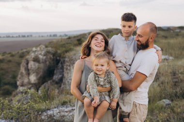 Neşeli bir aile dışarıda birlikte vakit geçiriyor. Ebeveynler çocuklarıyla birlikte gülümsüyor ve kırsal alandan zevk alıyorlar, mutluluğu ve birlikteliği kucaklıyorlar..