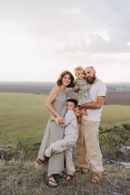 Neşeli bir aile açık bir alanda birlikte güzel anlar geçiriyorlar. Ebeveynler ve iki çocuk kucaklaşır, sevgi, mutluluk ve beraberlik sergilerler..