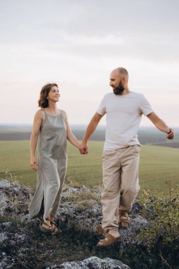 Bir çift, tepenin yamacında huzur içinde yürüyüp el ele tutuşarak huzurlu bir akşamda doğanın huzurunu kucaklıyor..