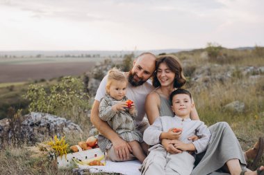 Güzel bir kırsal alanda piknik yapan neşeli bir aile. Çocuklu ebeveynler, doğa ve sükunetle çevrili kaliteli zaman geçirmekten hoşlanıyorlar..